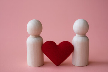 Red heart shape between wooden figurines of man and man on pink background. Love LGBTQ concept. Sexual minorities and communities concept