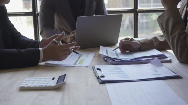 Group of Asian businessmen brainstorming close-up at plan meeting statistical analysis and pointing graph employee taking notes with laptop on table finance business success statistics concept