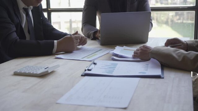 Group of Asian businessmen brainstorming close-up at plan meeting statistical analysis and pointing graph employee taking notes with laptop on table finance business success statistics concept