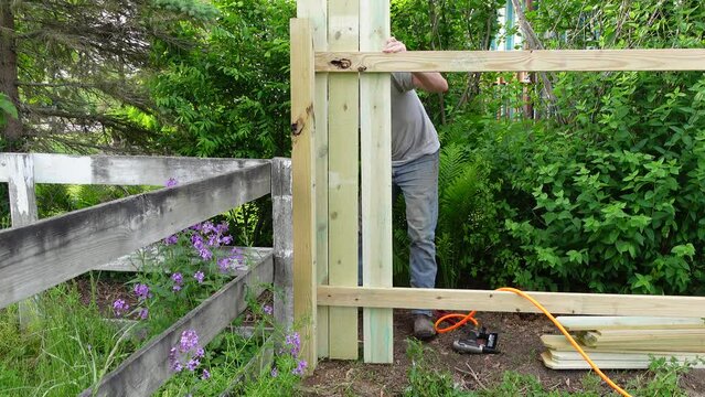 Man prepares plank and fix it with pneumatic nail gun for fence, static view