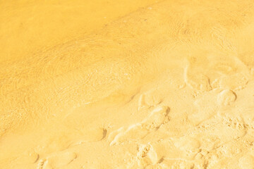 Golden sand on the beach with clear water. Close-up of crystal clear water near the sandy shore. Background on the theme of environmentally friendly recreation.