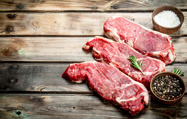 Raw marbled beef steaks with salt and aromatic spices.