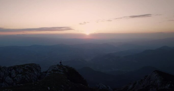 A drone shot of the top of mountain Peca in the early morning with a sunrise, hiker standing at the end of the mountain ridge.