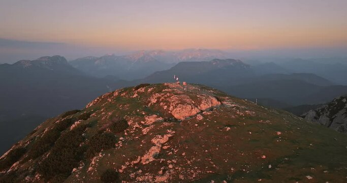 Drone shot of the top of mountain Peca at the sunrse where a hiker is holding a slovenian flag on the pole.