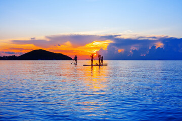 People silhouettes stand SUP paddle boarding, sea sunset beach, active young man woman surfing paddling board, ocean sunrise, surfboard, healthy lifestyle, water sport, summer holidays, relax vacation