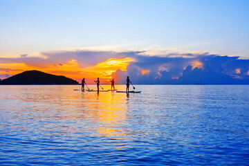 People silhouettes stand SUP paddle boarding, sea sunset beach, active young man woman surfing...