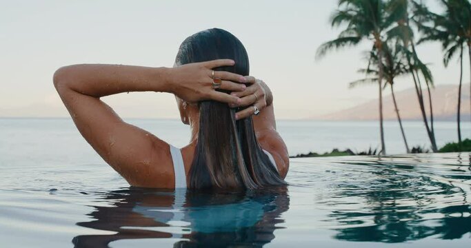 Beautiful woman relaxing in luxury infinity pool at tropical resort spa at sunrise on vacation
