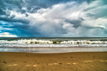 A sandy seashore with clouds. Background with the sky and the surf on the theme of beach holidays and sea travel.