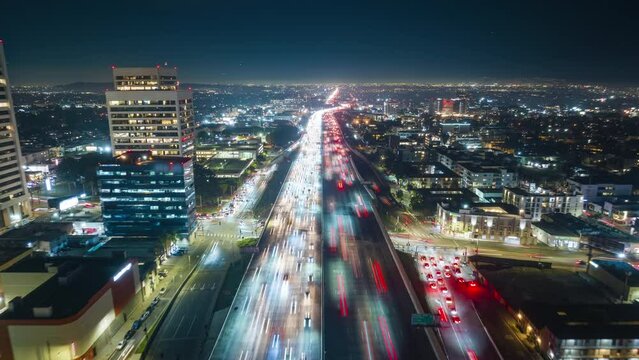Cinematic hyper lapse aerial footage zoom out flying back alone 405 busy highway at night. Rush hour with busy traffic in both ways on multiple lanes at Los Angeles cityscape and planes landing above