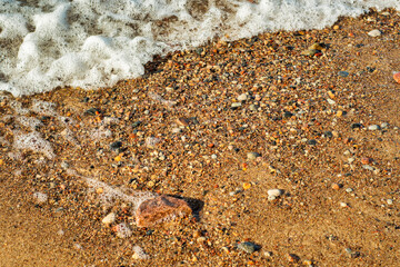 Small waves calmly run onto the pebbly shore. Background with an empty seashore on a warm summer day.