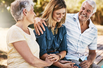 Senior couple in nature with their adult daughter sitting, talking and bonding together in a garden. Happy, love and elderly people embracing child with care, happiness and affection in outdoor park.