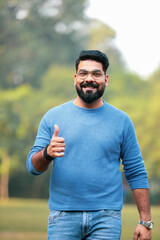 Young indian man showing thumps up at park.