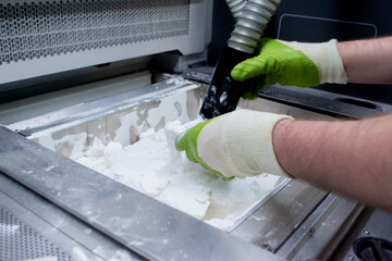 Male worker taking out models from white polyamide powder in working chamber of 3D printer,...