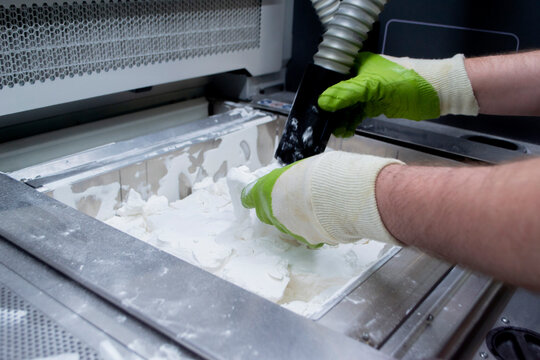 Male worker taking out models from white polyamide powder in working chamber of 3D printer, cleaning powder and putting on surface. Process of creating model on powder 3D printer. Multi Jet Fusion MJF