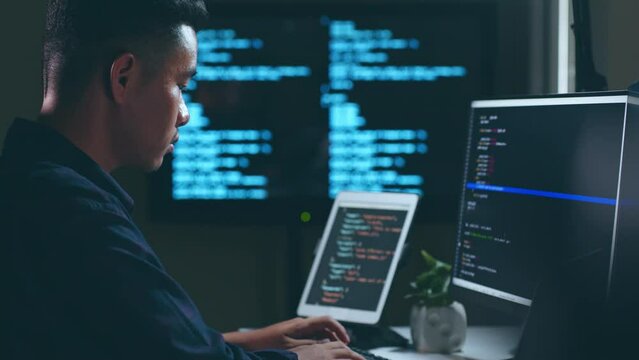 Young Asian man, developer programmer, software engineer, IT support, working hard at night overtime on computer to check coding in bugging system