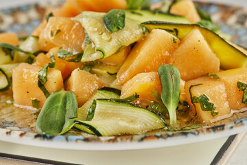 Salad with melon zucchini and herbs on white marble