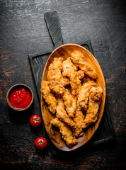 Chicken strips in a plate on a cutting Board with sauce and tomatoes.