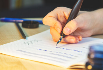 A girl sits at the table and writes with a pen and ink. Calligraphy, handwriting correction, beautiful writing.
