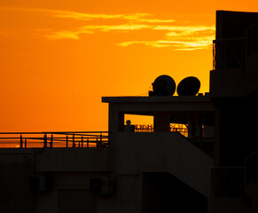 Silhouette of the roof of the house with an antenna on the background of the sunset.