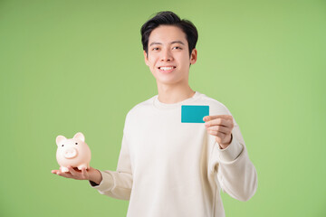 Image of young Asian man holding piggy bank on background