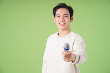 Image of young Asian man holding microphone on background