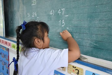 Primary Thai students are writing math answers on the chalk board in the classroom, The message...