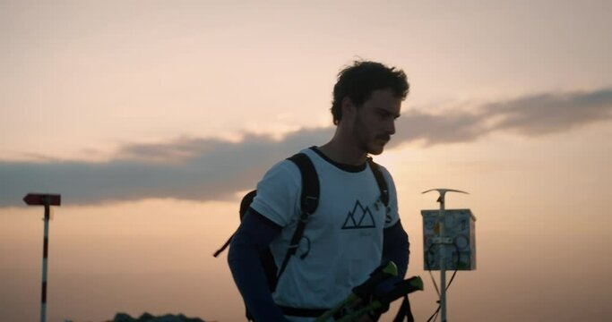 Hiker reching the top of mountain Peca, putting his gear away on the ground. Early morning sun on the sky with some clouds.