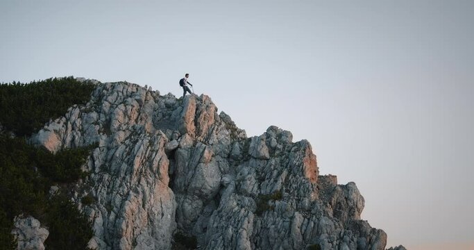 Shot of the hiker standing at the end of mountain ridge on mountain Peca in the early morning at the sunrise. Clear sky.