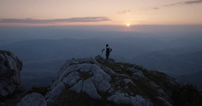 Hiker standing at the edhe of a mountain ridge to admire the early morning vive and the sunrise. Some clouds in the sky.