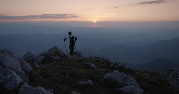 Camera tracking a young hiker who has topped at the edhge of a mountain ridge to admire a beautiful sunrise.