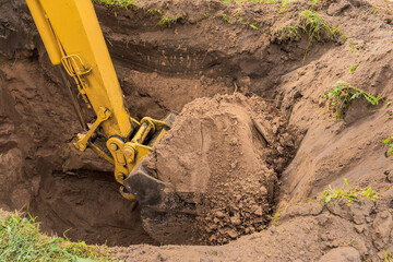 A bucket of excavator with a pile of earth digs a hole on the construction site. Industrial work