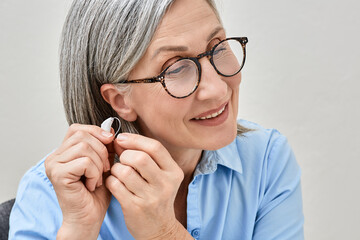 Grey-haired mature woman with hearing impairment using hearing aid. Hearing solutions for deafness people - 562322141