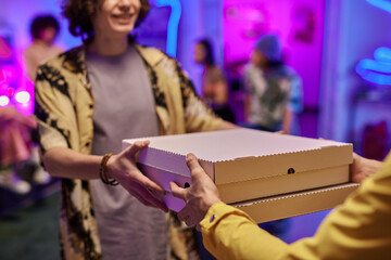 Close-up of young smiling man taking boxes with pizza passed by deliveryman in uniform against...