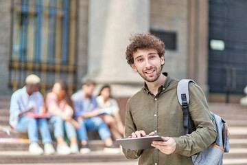 student using a digital tablet while standing in front of the university.