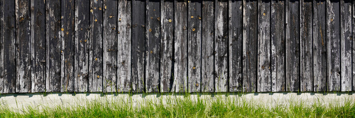 panoramic wooden wall background damaged fence old facade in web header panorama with the cement floor and weeds