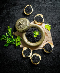 Fototapeta na wymiar Black caviar on bread slices and caviar in a bowl on paper with parsley.