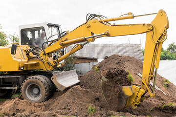 A hydraulic piston and a bucket excavator dig the ground next to a pile of sand on an industrial...