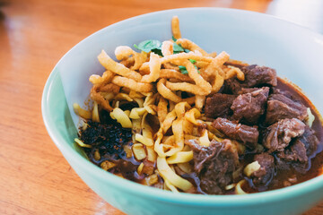 Front view of Khao Soi Thai style. Northern Thai Curry Noodles with Beef on wooden table at the restaurant. Recipe popular traditional Thai Asian style Lanna food. Copy space