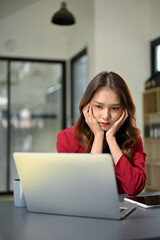 Unhappy and bored young Asian businesswoman sits at her office desk, feeling tired from work