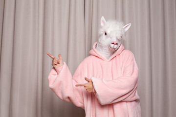 Person in pink hoodie with lama head pointing back on studio wall background