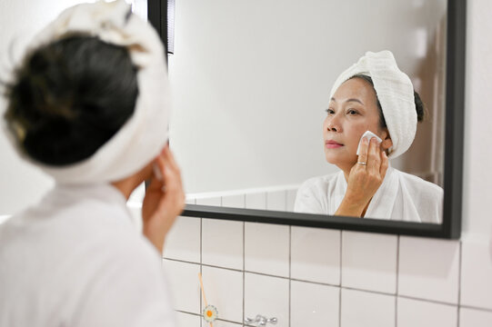 Attractive Mature Aged Asian Woman Removing Makeup, Looking In The Mirror. Beauty Night Routine