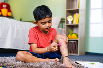 Preteen playful kid making drawings on leg using sketch pens at home - concept of childhood...