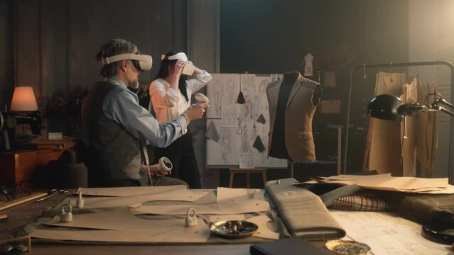 Tailors wearing VR headset with wireless controllers. They working in luxury atelier or tailoring workshop and creating weeding suit in virtual reality. Concept of technologies of future in business.