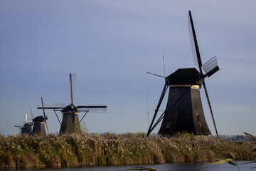 iconic windmills in Kinderdijk Netherlands next to canal waterway flood management. Landmark buildings originally made to pump water out of low land polder to preserve land reclaimed from the sea