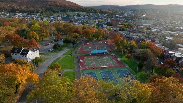 Aerial orbit around park with basketball courts in downtown of American city. Surrounded by colorful autumn foliage. Golden hour light.
