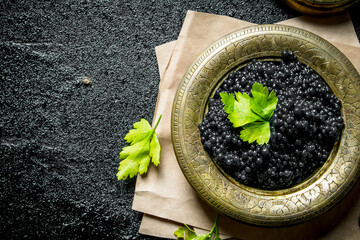 Black caviar in a bowl on paper with parsley.
