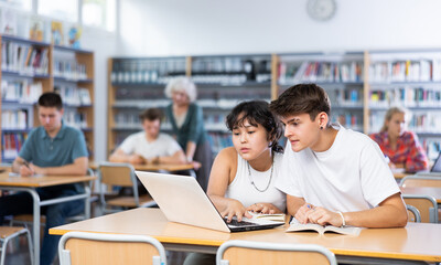 Boy and girl study together at laptop while sitting in a school library