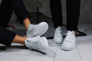 Summer shoes. Close-up of male and female legs in black pants and white casual sneakers. Summer...