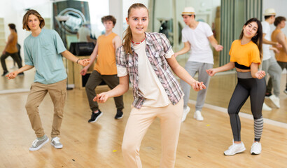 Smiling teenage girl dancer practicing active vigorous dance with group in modern studio. - obrazy, fototapety, plakaty