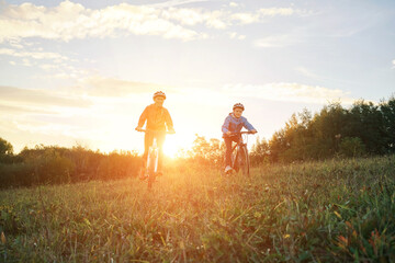 Fototapeta na wymiar Mother and son ride a bike. Happy cute boy in helmet learn to riding a bike in park on green meadow in autumn day at sunset time. Family weekend. 